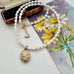 A white pearl beaded necklace with an oval rolled gold engraved vintage locket, displayed diagonally over a vintage floral card featuring yellow daisies.