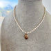 A necklace of irregular white pearls with a small oval vintage rolled gold locket, displayed on a gray felt jewelry bust.
