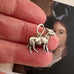 Vintage silver goat charm held between fingers with a blurred background