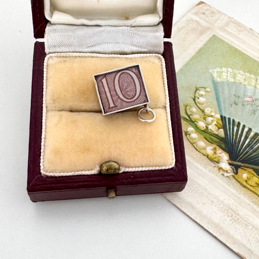 A vintage emergancy money 10 shilling silver pendant , displayed inside an open antique presentation box next to an old illustrated card.
