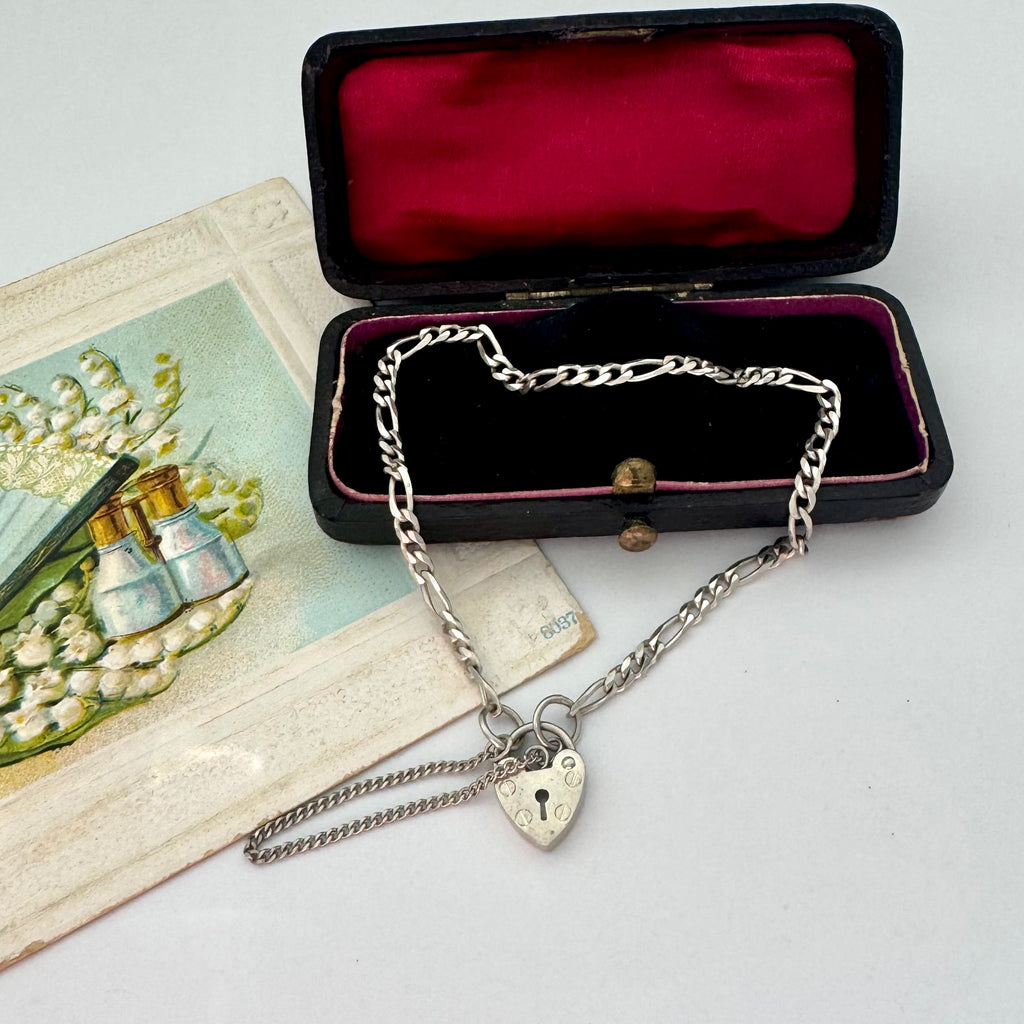 Silver bracelet with a heart-shaped clasp in an open jewelry box on a white surface.