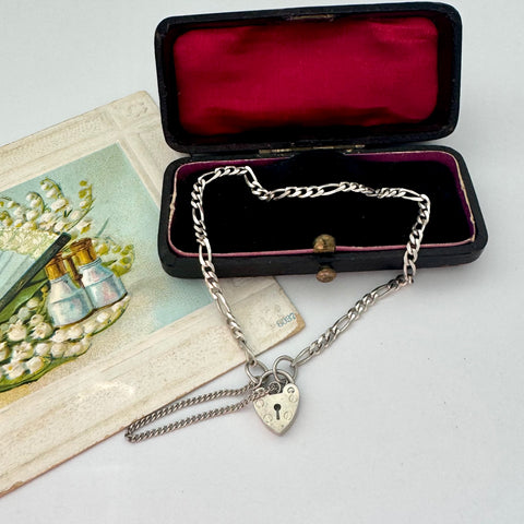 Silver bracelet with a heart-shaped clasp in an open jewelry box on a white surface.