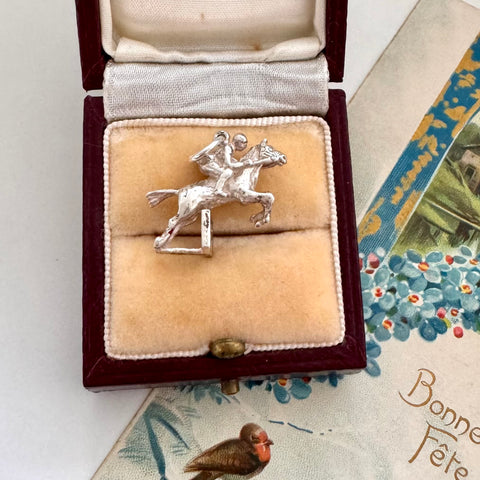 Vintage silver equestrian charm in a jewelry box on an old letter with decorative elements.