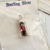 A miniature sterling silver pendant shaped like a guardhouse with a tiny figure inside wearing a red uniform, displayed on its white backing card labeled 'Sterling Silver'.