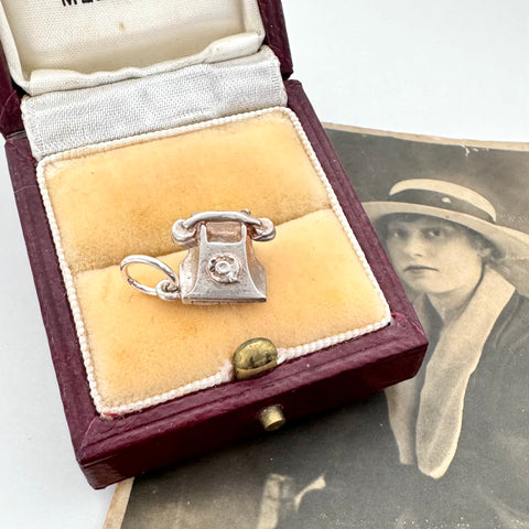 Silver phone charm in a jewelry box with an old photograph of a woman in the background