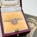 Back of silver telephone charm in an open jewelry box, with a vintage photo of a woman in the background.