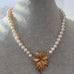 A pearl necklace with a gold-toned flower pendant, displayed on a gray jewelry bust.
