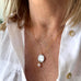 Image of a woman wearing Vonk Jewellery antique coin and pearl necklace and a whit linen shirt